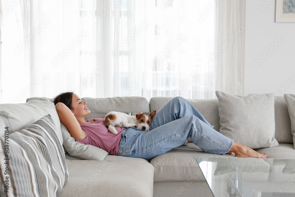 Portrait of young beautiful woman lying on the couch with her adorable wire haired Jack Russel terrier puppy. Loving girl with rough coated pup having fun. Background, close up, copy space. Portrait of young beautiful woman lying on the couch with her adorable wire haired Jack Russel terrier puppy. Loving girl with rough coated pup having fun. Background, close up, copy space.