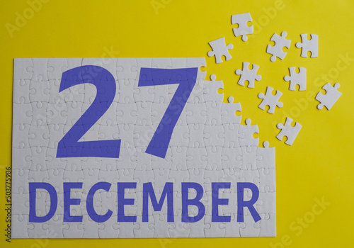27 december calendar date on a white puzzle with separate details. Puzzle on a yellow background with a blue inscription
