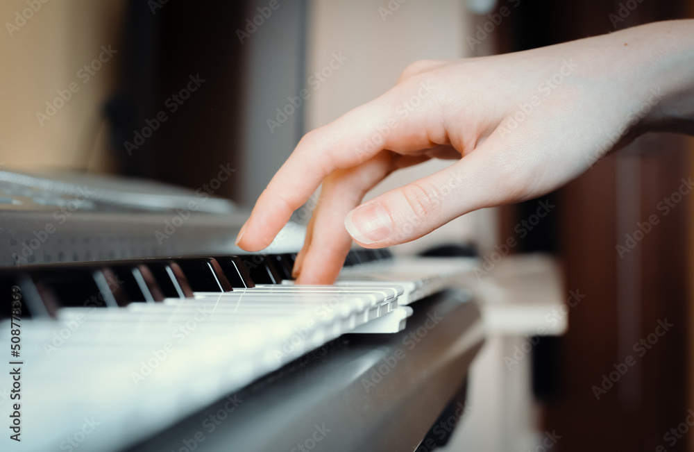 Female hand presses the keys of a synthesizer, selective focus, side view