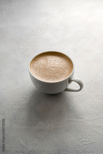 Cup of coffee on textured grey background. Lifestyle photo with natural light. Minimalistic style with cup of coffee and milk foam.