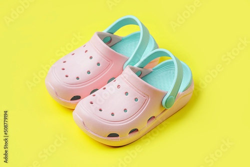 Pink kids clogs beach slippers on yellow background. Summer vacation concept. Fashion Sandals Beach Flip-Flops