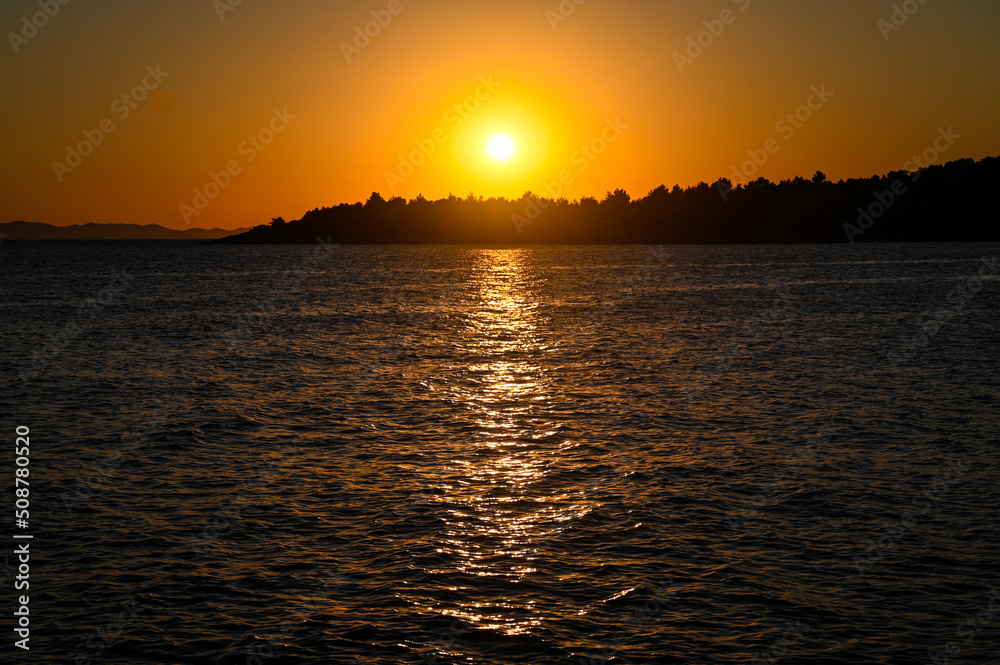 Golden sunset at the sea with soft waves. Tropical sunset. Seascape and shore. Sun going down in orange sky over horizon. Silhouette of a island.