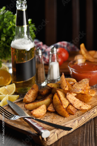 Rustic spicy fried potato slice on a wooden plate, with tomato sauce and beer