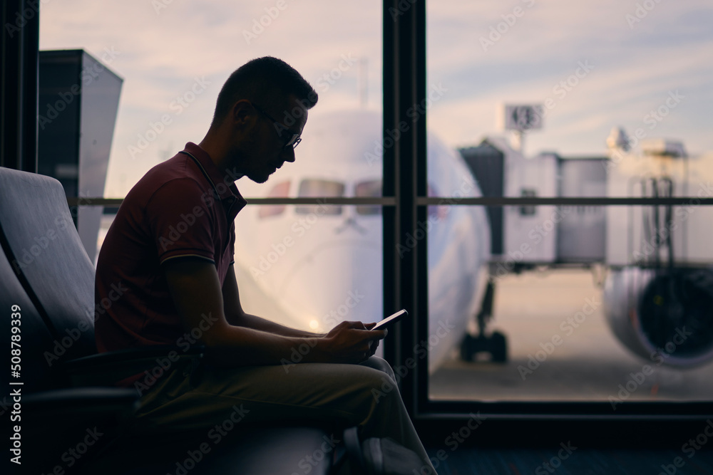Silhouette of young man waiting while waiting for flight. Traveler using phone in airport terminal. . Silhouette of young man waiting while waiting for flight. Traveler using phone in airport terminal. .