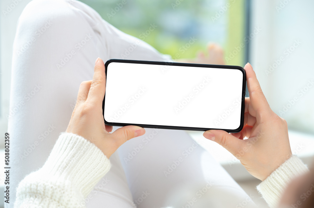 Woman lies in relaxed position and watches video content on cellphone or mobile smartphone. holding phone horizontally Woman lies in relaxed position and watches video content on cellphone or mobile smartphone. holding phone horizontally