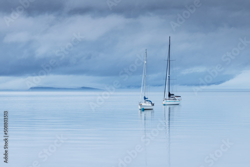 two sailboats anchored at low tide in blue hour in Brodick Bay, Isle of Arran, Scotland, United Kingdom