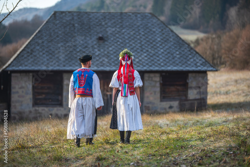 A couple dressed in traditional folk costume. Slovak costume in autumn nature. Old country cottage in the background. Young couple in folk costume walking in the garden photo