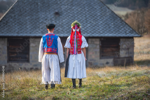 A couple dressed in traditional folk costume. Slovak costume in autumn nature. Old country cottage in the background. Young couple in folk costume walking in the garden