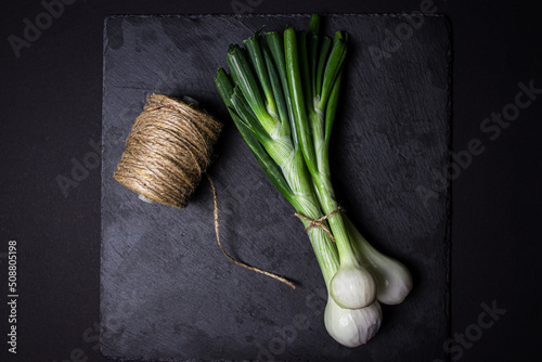 Foto Fresh green onion on a black background. Useful vegetable.