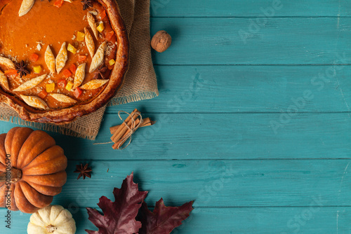 top view of pumpkin pie on wooden turquoise background decorated with autumn leaves and pumpkin