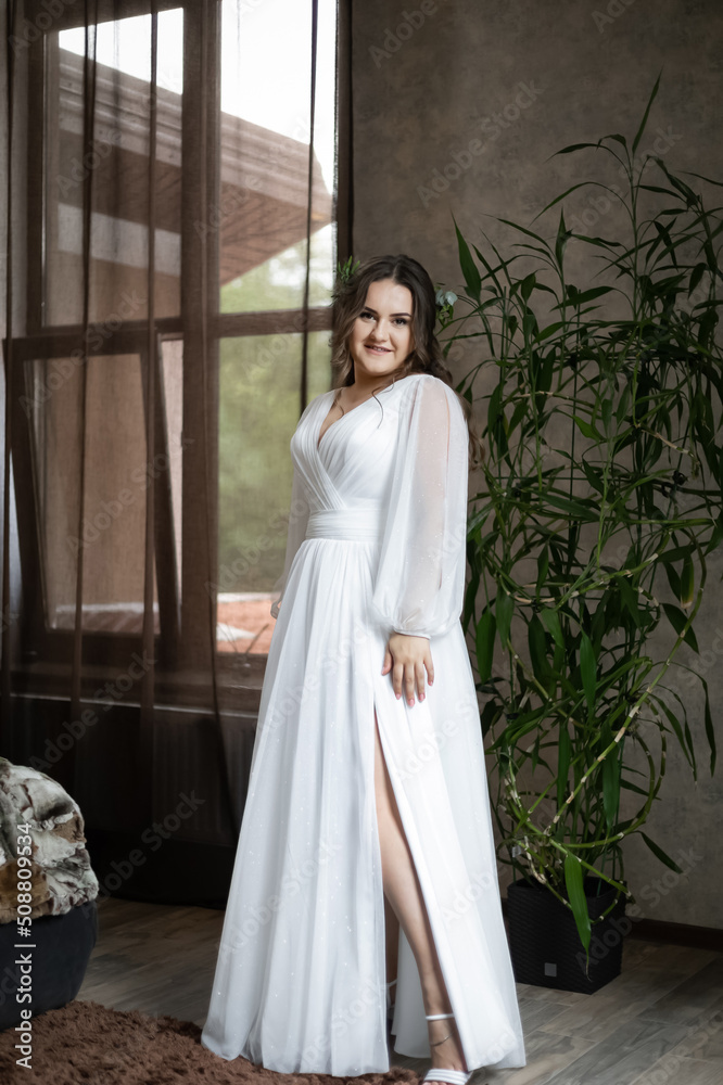 Fototapeta premium A lush, charming bride in the room. Stylish girl in a wedding dress with a bridal bouquet.