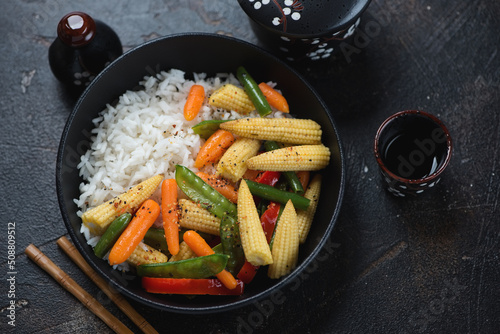 Rice bowl with vegetable stir-fry on a dark-brown stone background, elevated view, horizontal shot