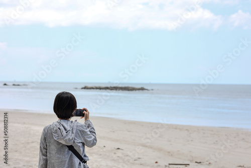 Asian woman use smartphone taking sea view and roadside photos in southern Thailand. Travel vacation concept. 