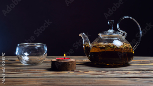 Hot herbal tea in glass teapot on wooden table on dark background. Traditional herbal drink. Place for text or design.
