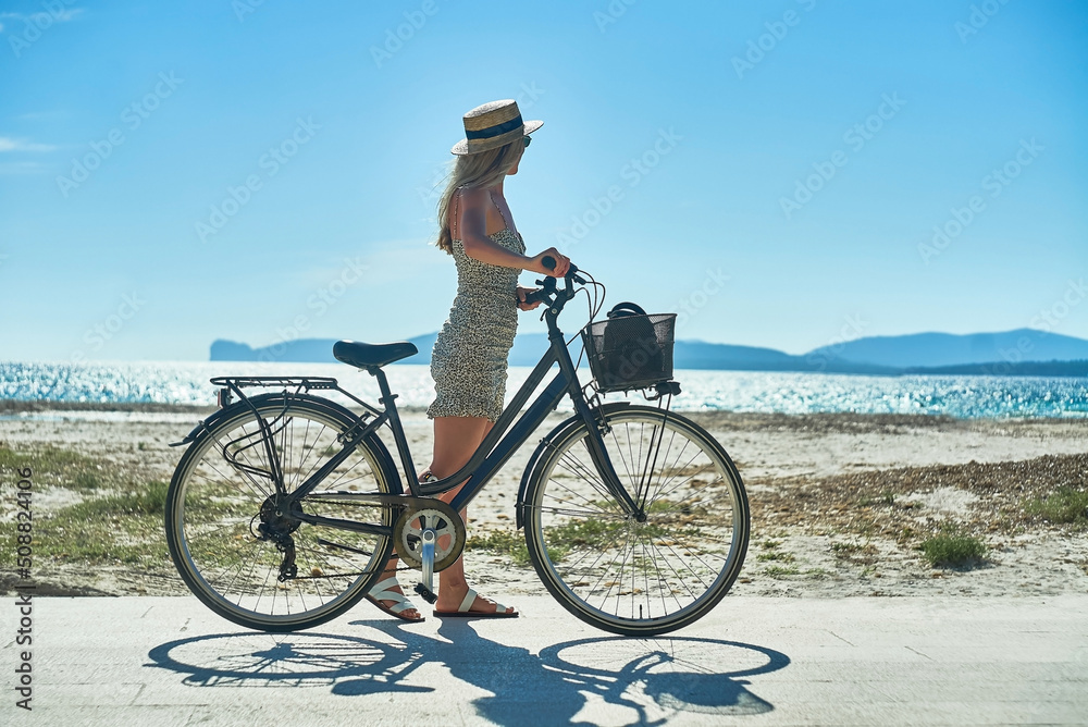 Fototapeta premium Carefree woman with bike riding on sand beach having fun, on the seaside promenade on a summer day.