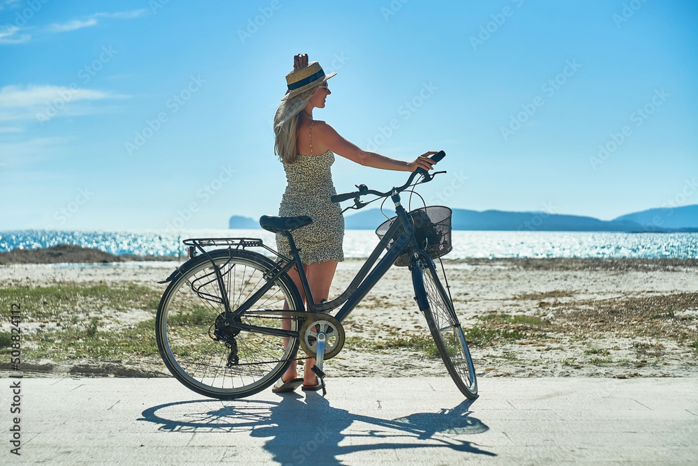 Obraz premium Carefree woman with bike riding on sand beach having fun, on the seaside promenade on a summer day.