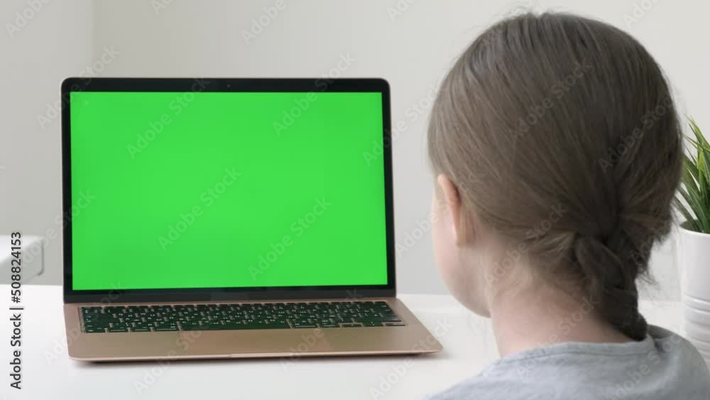 School girl studying during online lessons at home in front of green screen laptop, back view. Chroma key, e-learning, webinar. Online distance education for children. Back to school School girl studying during online lessons at home in front of green screen laptop, back view. Chroma key, e-learning, webinar. Online distance education for children. Back to school