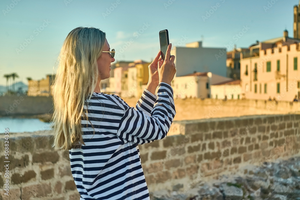 Woman traveler tourist using smartphone, taking photo of sea view at sunset in summer day. Enjoying European, Famous popular touristic place in world.
