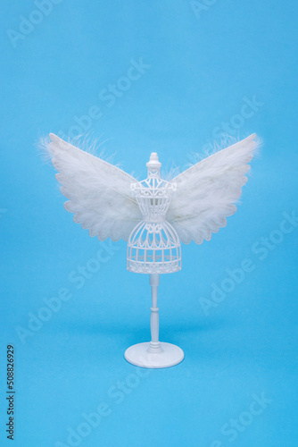 The white female tailor doll with an angel wings isolated on a pastel blue background. Minimal fashion concept. Side view, soft shadows. photo