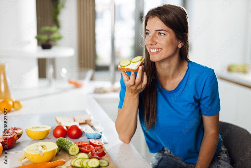 Happy woman eating a sandwich in the kitchen Happy woman eating a sandwich in the kitchen