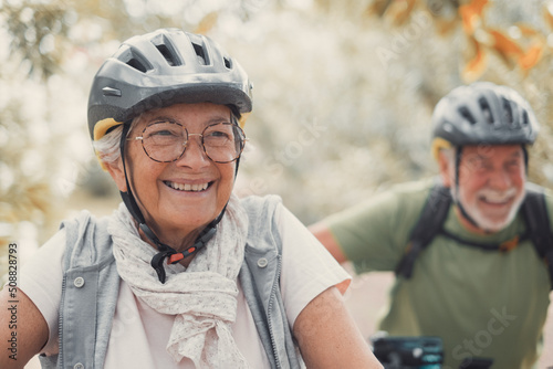 Portrait of one old woman smiling and enjoying nature outdoors riding bike with her husband laughing. Headshot of mature female with glasses feeling healthy. © Daniel