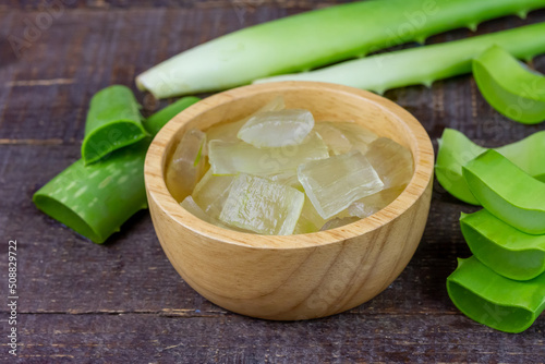 Aloe vera gel in wooden bowl with fresh aloe vera on rustic wooden background.