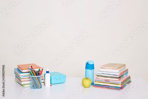 Indoor shot of school supplies: books, pen holder, fresh apple, bottle of water, pens, pencils, working area for little students, isolated over white background.