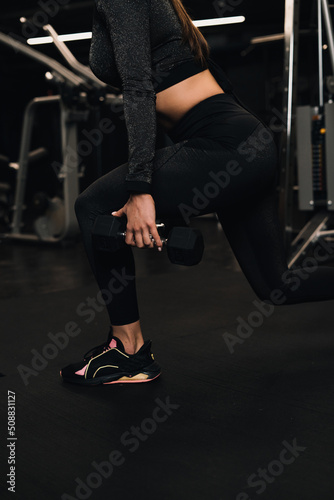 girl athlete doing squats with dumbbells in the gym. dark background