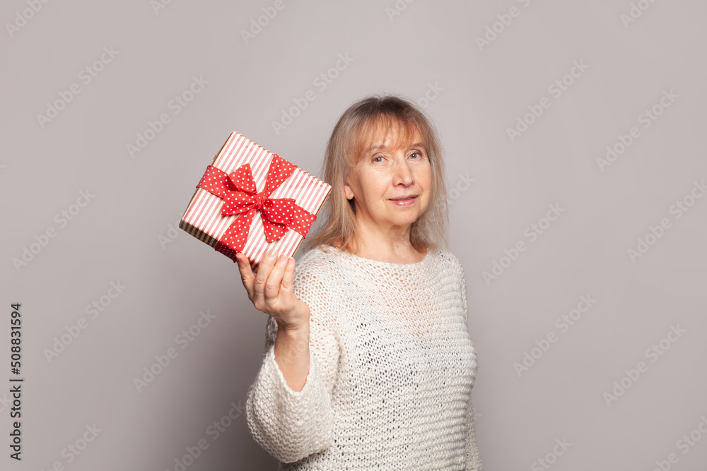 Happy senior woman holding red and white gift box Happy senior woman holding red and white gift box