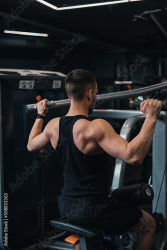 guy athlete shakes his back on the simulator in the gym. dark background