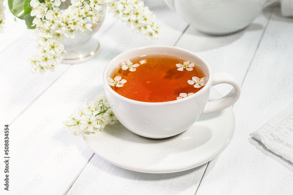 Useful spring tea with bird cherry in a white cup on a light background Useful spring tea with bird cherry in a white cup on a light background