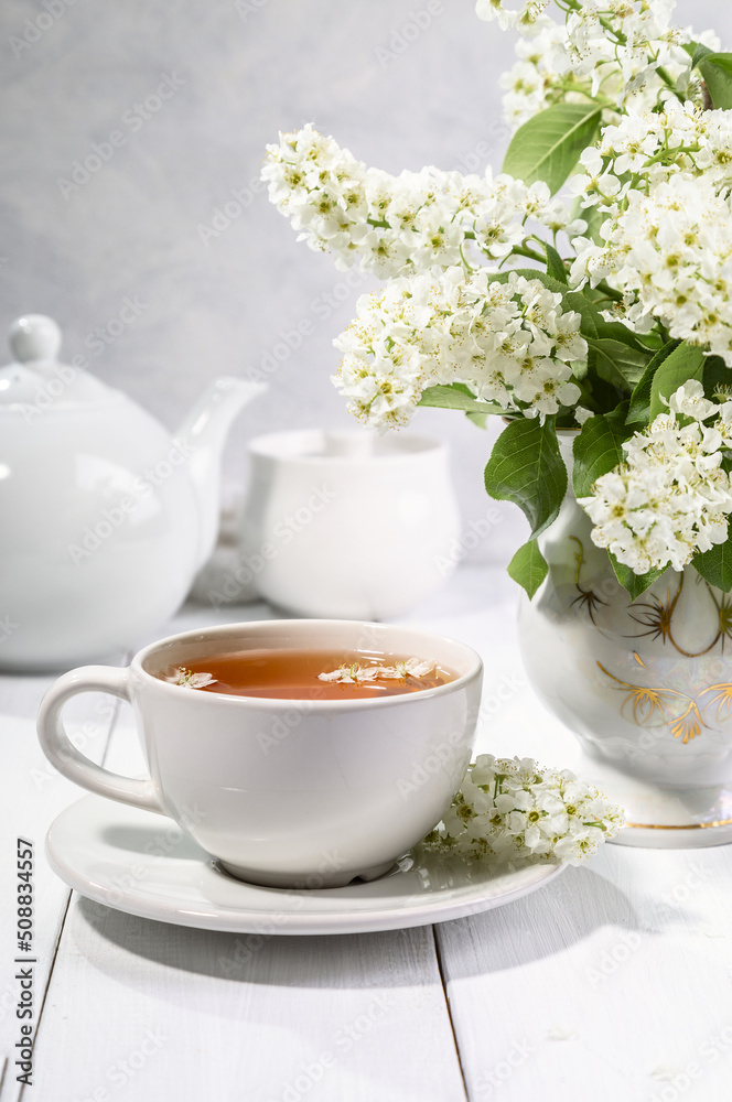 Useful spring tea with bird cherry in a white cup on a light background Useful spring tea with bird cherry in a white cup on a light background