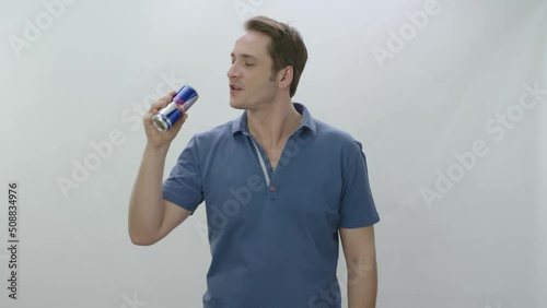 Young man drinks fizzy RedBull beverage from metal bottle. Slow motion video. The young man drinks RedBull and is happy to cool off. Slow motion video. Indoor studio isolated on white background.