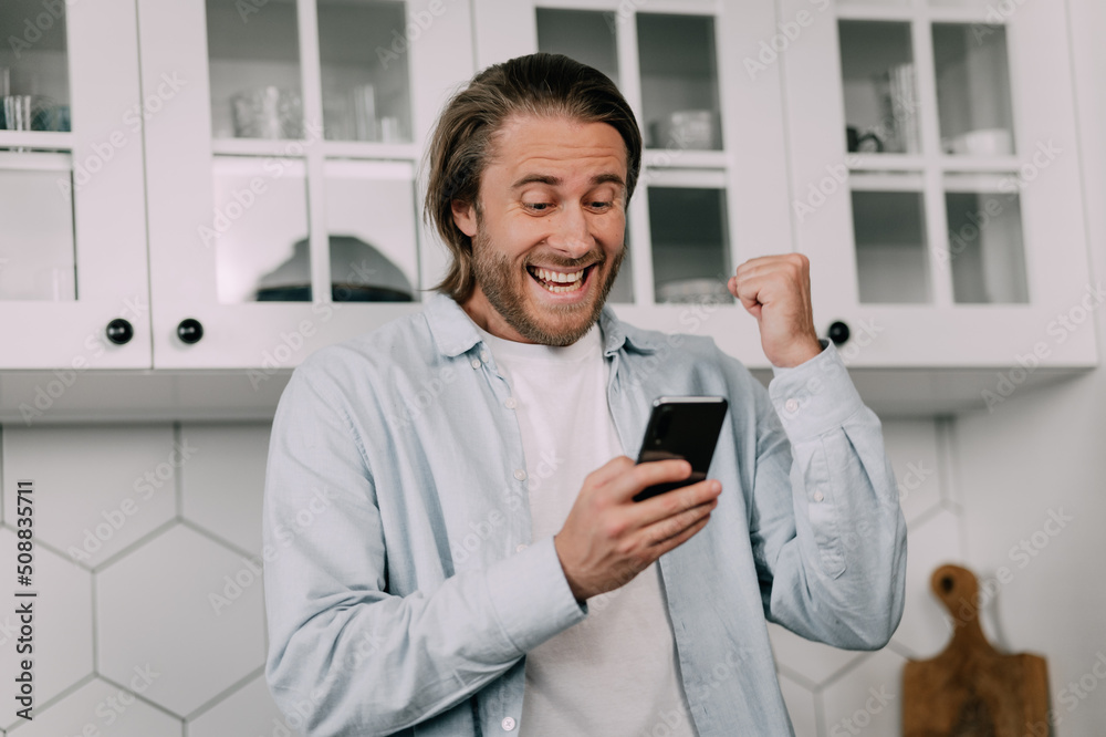A young man rejoices in success looking at his smartphone at home. Lucky bet, stock market, crypto market A young man rejoices in success looking at his smartphone at home. Lucky bet, stock market, crypto market