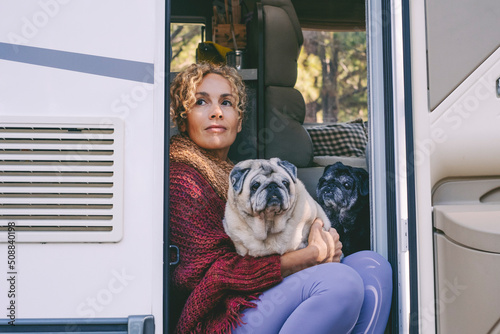 Photography Cute adult woman sitting and relaxing on the door of her camper van with her two pug dogs