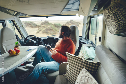 Fototapeta Adult man relaxing after trip with camper van parked free with beach view