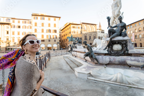 Young woman traveling famous italian landmarks in Florence city. Enjoying beautiful architecture and Neptuine fountain on Signoria square. Woman dressed in Italian style with colorful scarf in hair