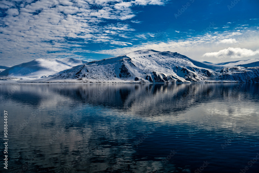 2022-05-15 BEAUTIFUL SNOW COVERED MOUNTAIN RANGE WITH SOME EXPOSED ROCKS WITH A REFLCTION IN THE WATER IN THE ARCTIC NEAR SPITSBERGEN NORWAY