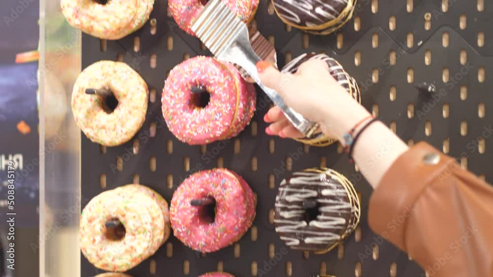  female hand takes with tongs a fresh sweet glazed donut in a bakery shop.dessert is sweet on the counter in cooking. woman buying fresh donuts