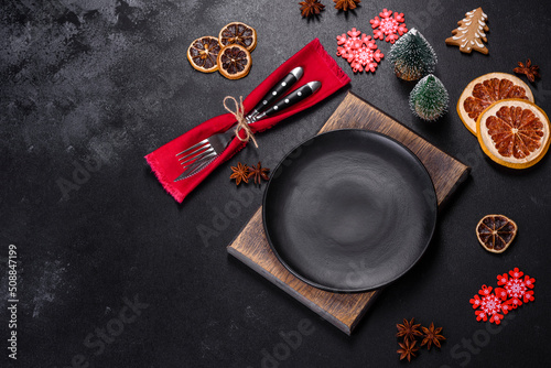 Christmas table setting with empty black ceramic plate, fir tree and black accessories