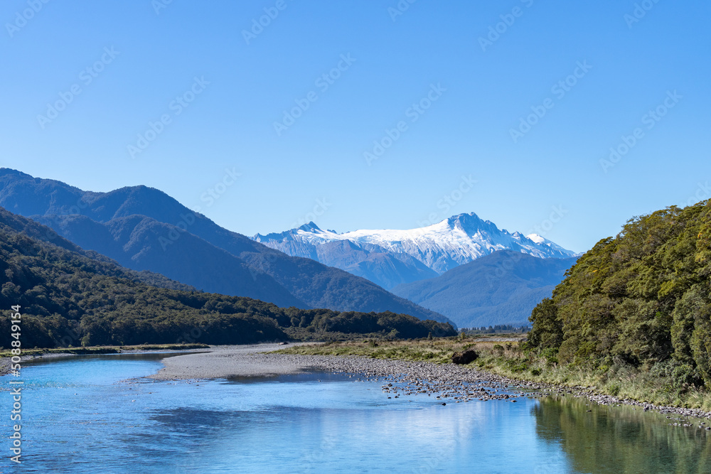 Makarora River flows over wider river bed between bush-clad South Alps mountains.