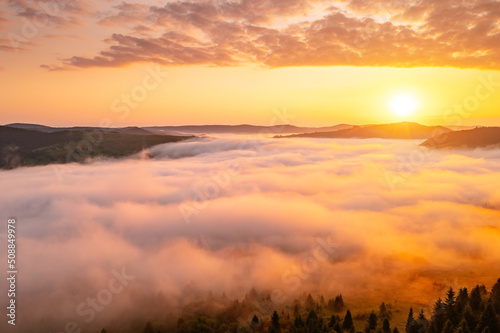 Bright thick fog covers the mountains in the rays of morning light.