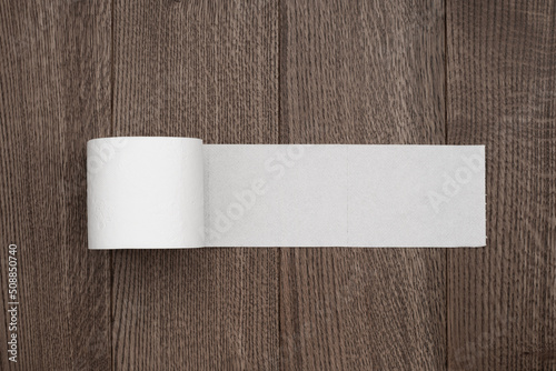 a roll of toilet paper on a wooden background is unwound with a place for an inscription or text copy space