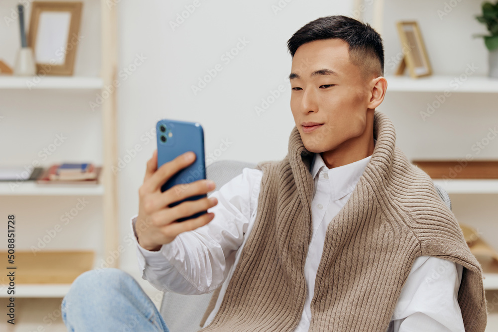 Asian man communication with the phone in his hands sits on a chair interior isolated background Asian man communication with the phone in his hands sits on a chair interior isolated background
