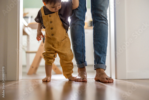  Little baby boy learning to walk with his father beside him at home 
