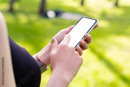 Redhead sportive woman wearing black sports bra standing on city park, outdoors hands holding phone with mockup white blank display, empty screen for social media. Mobile app tech concept. photo