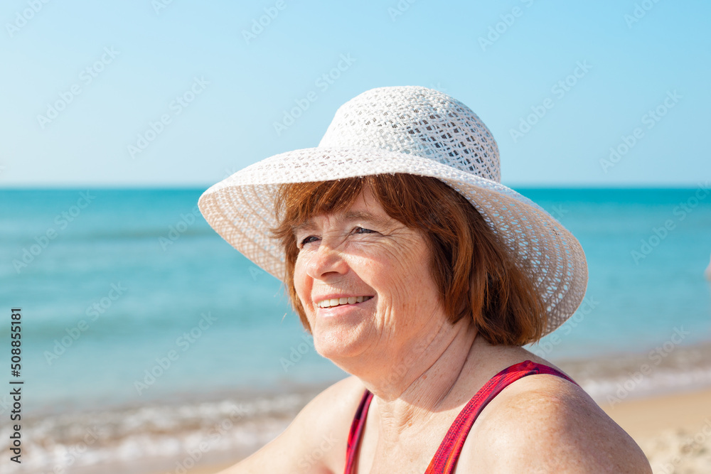 An elderly woman in a hat laughs on the seashore on a sunny day, close-up.Happy summer days