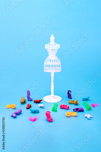 Female sewing doll with pile of shoes against blue seamless background. Minimalistic fashion concept. Side view photo