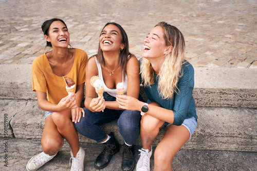 Fototapeta Three young woman eating ice cream cones and laugh good hot summer day during their vacation