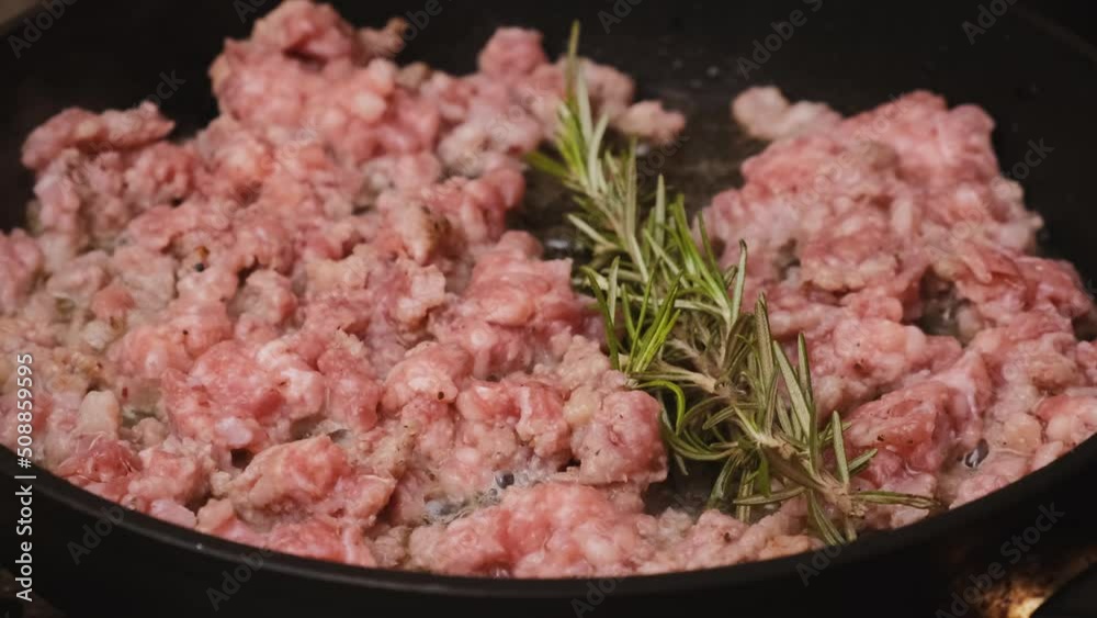 Hand puts rosemary to the raw minced meat frying in the frying pan. Cooking food concept. 4k video Hand puts rosemary to the raw minced meat frying in the frying pan. Cooking food concept. 4k video